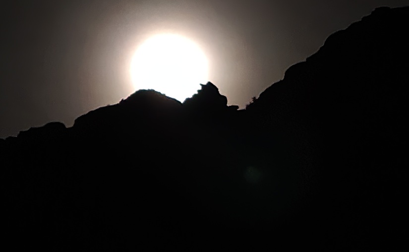 Moon resting atop dark canyon wall